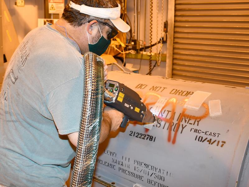 Bub King, combined trades worker, removes a swath of coating from an aircraft engine container during a demonstration of laser ablation technology held at FRCE.