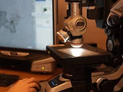 An engineer uses a microscope to examine corrosion pits on clad aluminum test panels. The work helped identify the chemical reaction between paint pigments and stripper components that caused the damage, using a material representative of the aluminum fuselage skin. (Maddie Chesbro-Crisalli photo © Boeing)