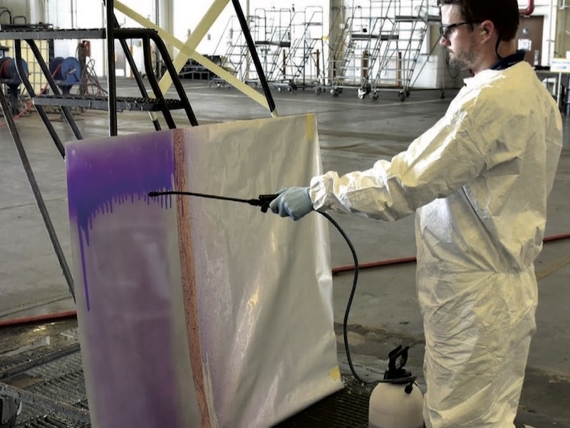 Spray application of eTCP ready-to-use at FRC Southeast to an aluminum panel. Production environment and panel orientation mimic spray conversion coating on aircraft as it is performed at FRC Southeast. (Photo Credit: Sjon Westre)