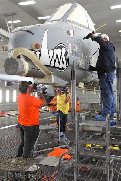 Anthony Montanez, Dennis Reeves and Brady Ringel, 576th Aircraft Maintenance Squadron technicians, prepare the first production A-10 Thunderbolt II for paint removal using a new robotic media blast technology Dec. 4, 2019, at Hill Air Force Base, Utah. The corrosion control technicians seal up the seams and holes in the outer-surface skin to prevent the blast media from entering the aircraft. (U.S Air Force photo by Todd Cromar)