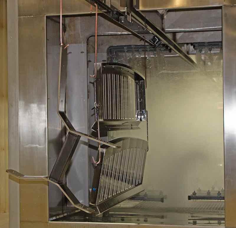 The system has a 4-stage wash, a dry-off oven, one topcoat booth, two cure ovens on parallel tracks, and then back to unload.