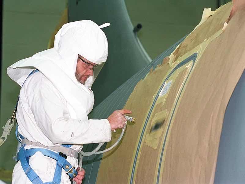 A man wearing protective gear painting a military plane.